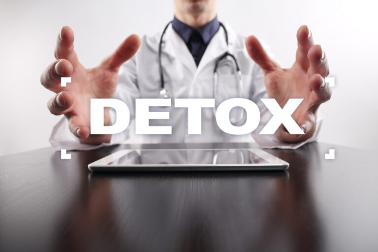 Doctor with hands outstretched over a tablet, with the word DETOX displayed.