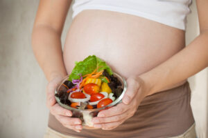 Pregnant woman holding a bowl of fresh salad with vegetables.