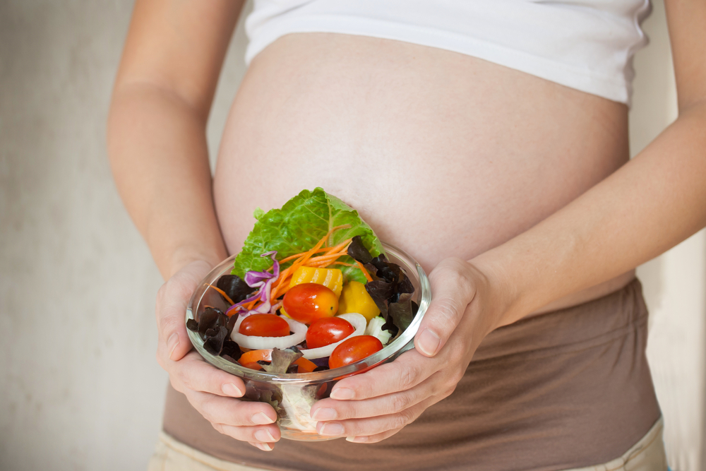 Pregnant woman holding a bowl of fresh salad with vegetables.