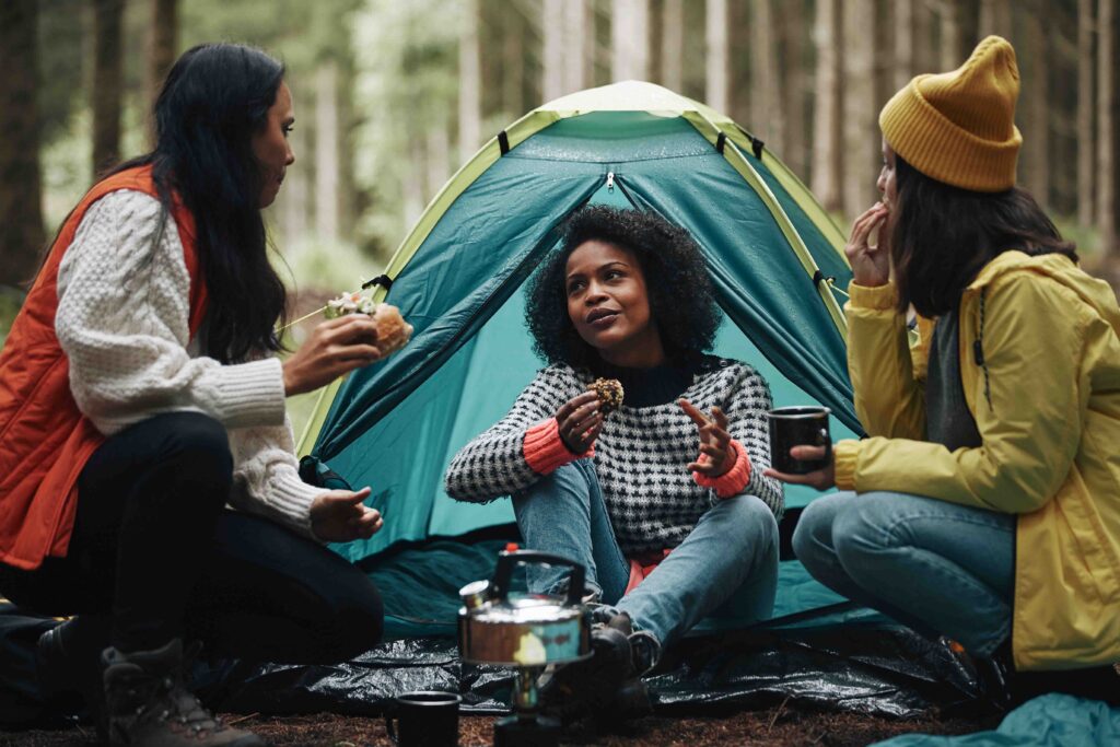 Three women talking by a tent in the mountains.