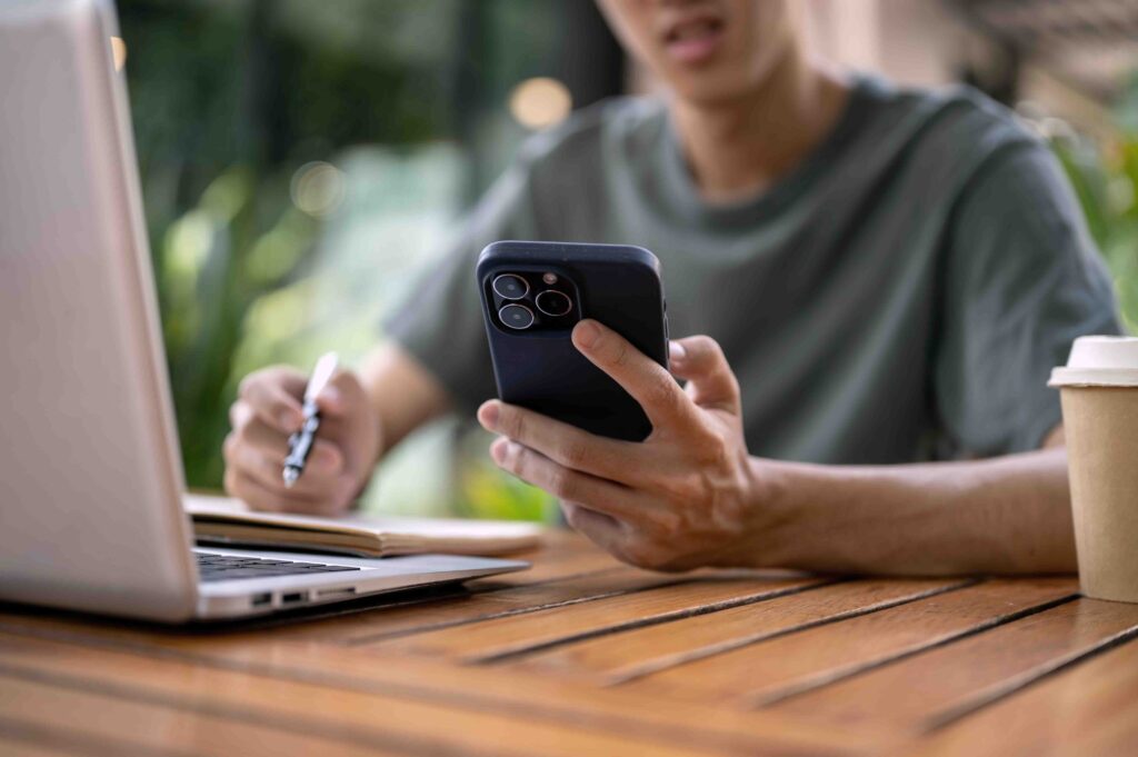 Person sitting at a table with laptop and phone making an appointment with a doctor.